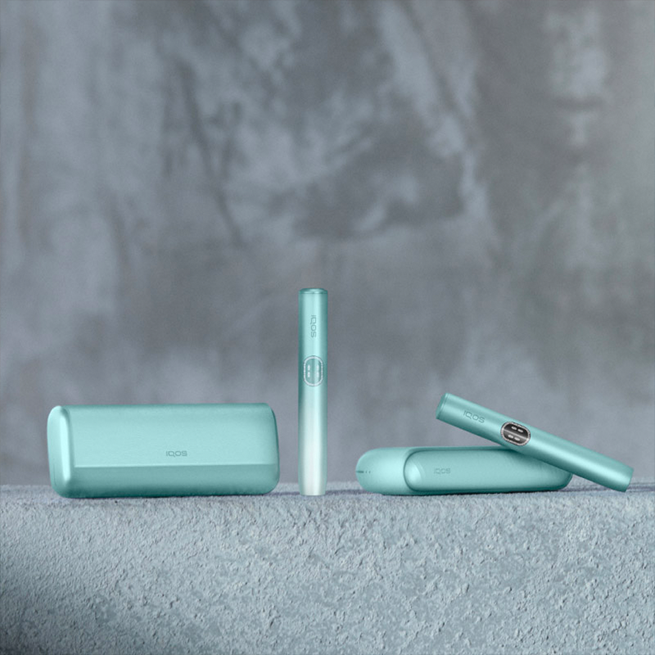 Three IQOS ILUMA i devices in different colors in a blurred colorful background.