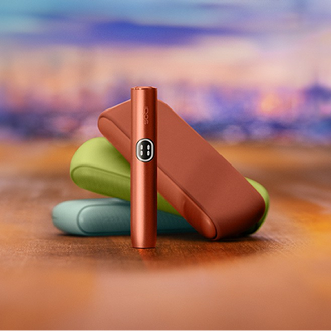 Three IQOS ILUMA i devices in different colors in a blurred colorful background.