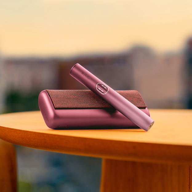 IQOS ILUMA i PRIME цвета Garnet лежит на деревянном столе на размытом фоне.